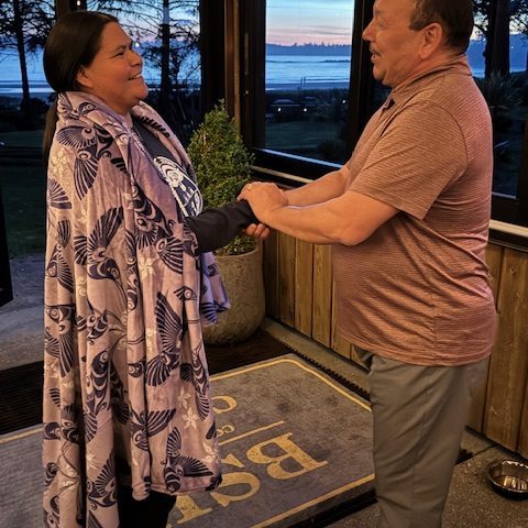 Two people shaking hands near a window with a sunset view.