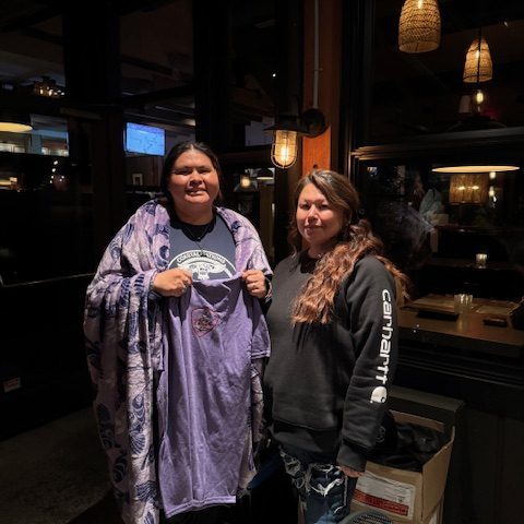 Two people indoors, one holding a purple shirt with a design.